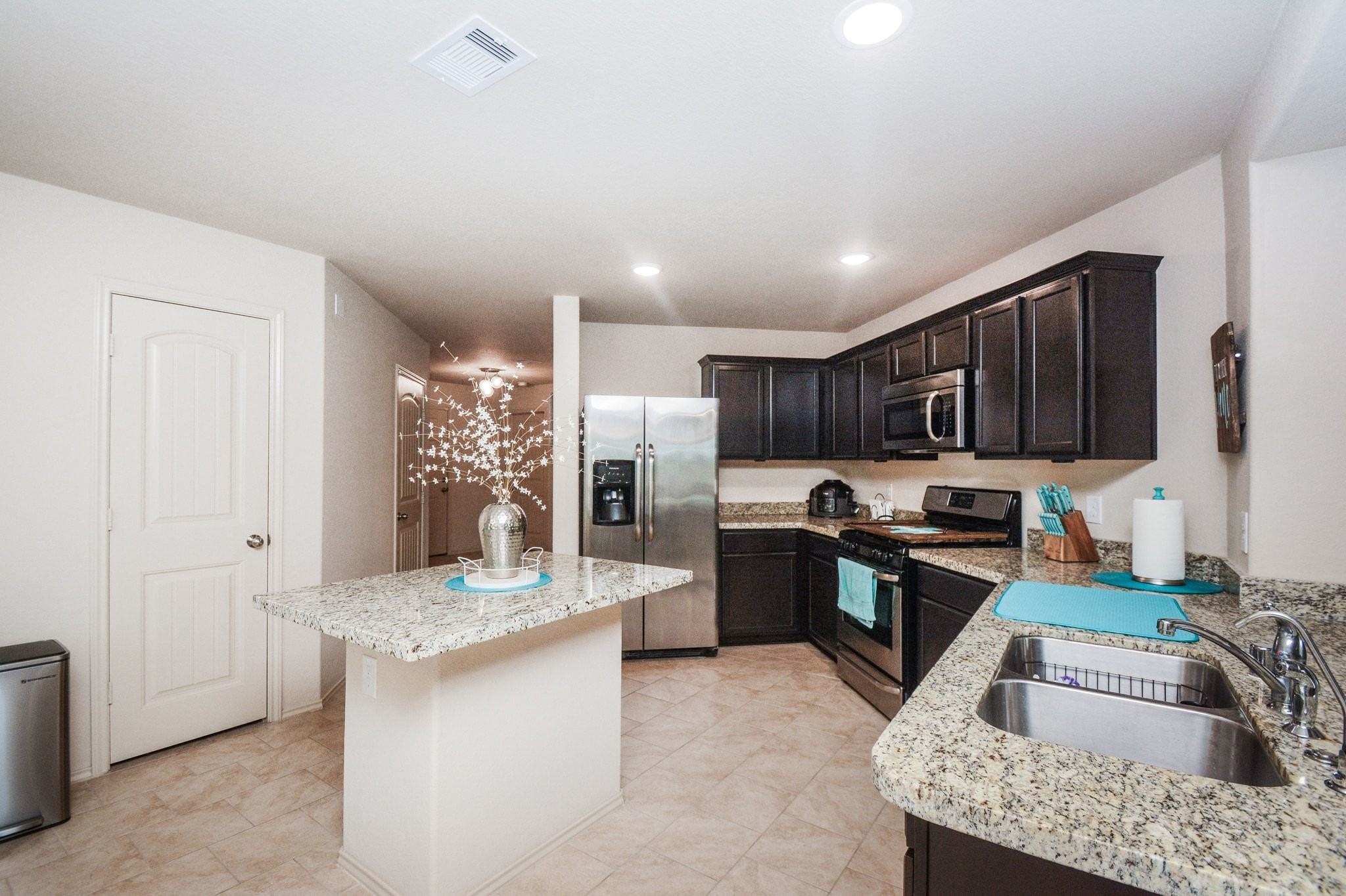 23318 Dukes Run Drive Spring, TX 77373 - Photo 7 of 41 This kitchen features dark wood cabinets, stainless steel appliances, and granite countertops. It includes a central island and a double sink, all set on light tile flooring, creating a modern and functional cooking space.