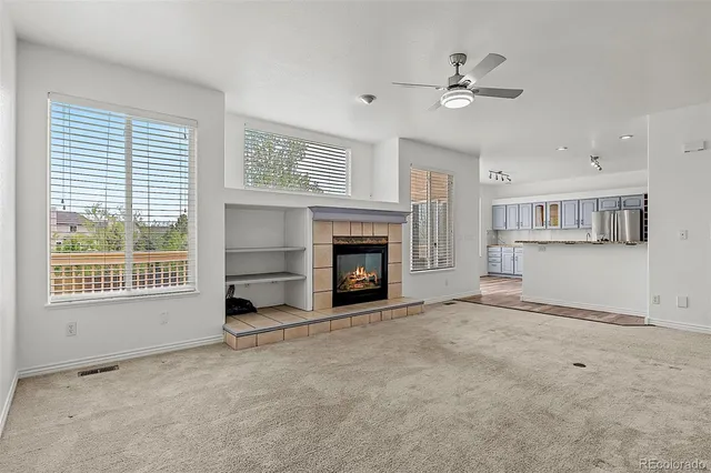 a view of a livingroom with a fireplace a ceiling fan and windows