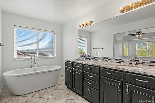 a bathroom with a granite countertop tub a double vanity sink a window and a mirror