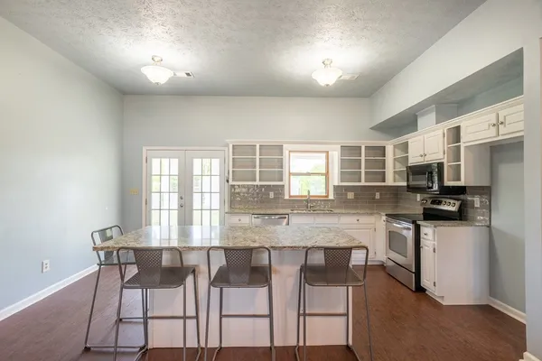 a kitchen with stainless steel appliances granite countertop a stove a sink dishwasher a refrigerator with white cabinets and wooden floor