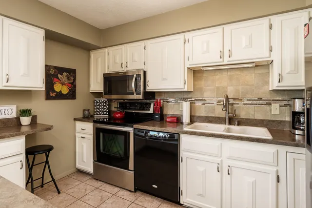 a kitchen with granite countertop white cabinets white appliances a sink and a large window
