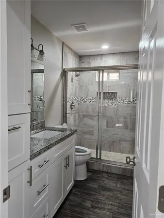 a bathroom with a granite countertop sink a toilet a mirror and shower