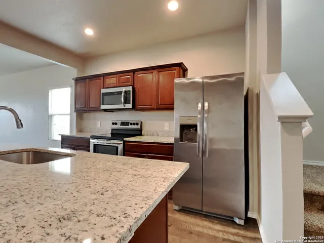 a kitchen with stainless steel appliances granite countertop a refrigerator a stove and a sink with wooden cabinets