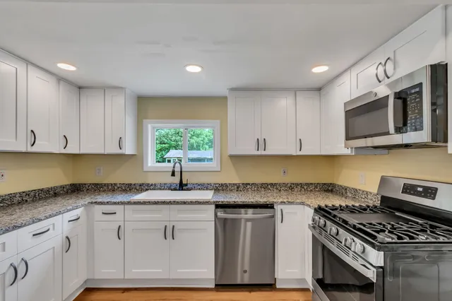 a kitchen with granite countertop a sink cabinets stainless steel appliances and a window