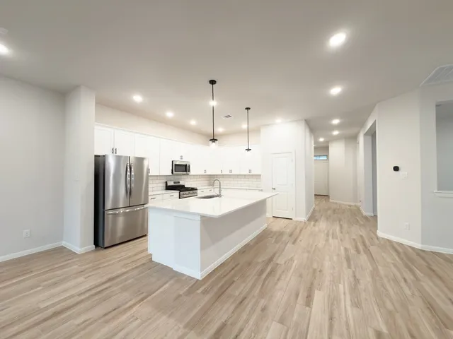 a large white kitchen with a refrigerator a sink dishwasher a stove and white cabinets with wooden floor