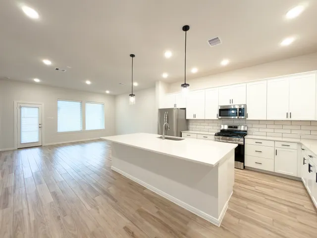 a large kitchen with kitchen island a stove a sink a refrigerator and white cabinets with wooden floor