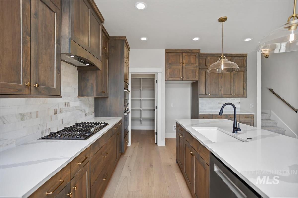 232 South Fusion Avenue Kuna, ID 83634 - Photo 11 of 50 Kitchen with light wood finished floors, stainless steel appliances, tasteful backsplash, light stone counters, and pendant lighting