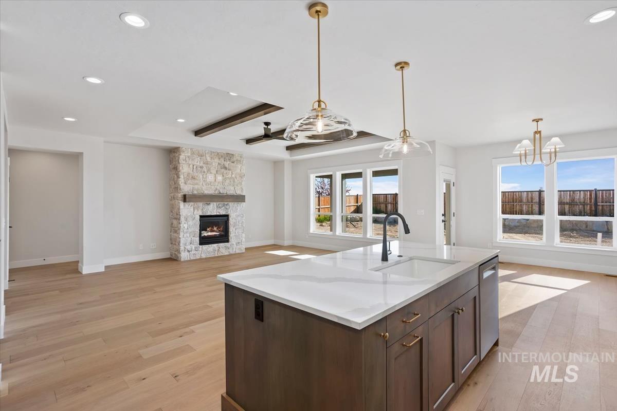 232 South Fusion Avenue Kuna, ID 83634 - Photo 47 of 50 Kitchen featuring dark wood finish cabinets, open floor plan, hanging light fixtures, a stone fireplace, and a tray ceiling