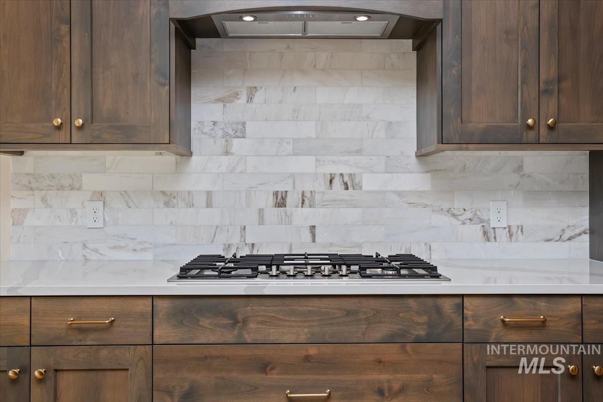 232 South Fusion Avenue Kuna, ID 83634 - Photo 13 of 50 Kitchen featuring dark wood finish cabinets, exhaust hood, stainless steel gas cooktop, and light stone countertops