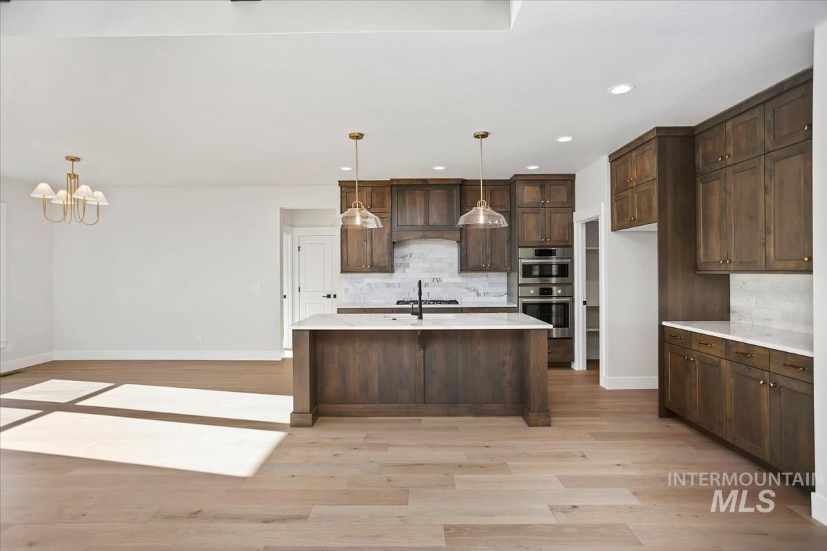232 South Fusion Avenue Kuna, ID 83634 - Photo 7 of 50 Kitchen featuring light stone countertops, dark wood finish cabinetry, tasteful backsplash, stainless steel double oven, and light wood-type flooring