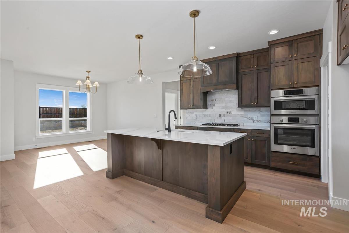 232 South Fusion Avenue Kuna, ID 83634 - Photo 8 of 50 Kitchen featuring dark wood finish cabinets, light stone counters, stainless steel appliances, and light wood-style floors