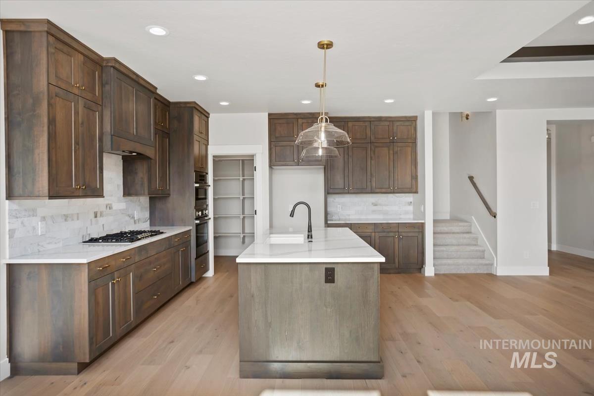 232 South Fusion Avenue Kuna, ID 83634 - Photo 9 of 50 Kitchen with light stone countertops, backsplash, light wood-style floors, and an island with sink