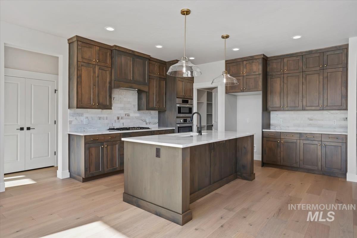 232 South Fusion Avenue Kuna, ID 83634 - Photo 10 of 50 Kitchen featuring light wood-style floors, dark wood finish cabinets, light stone countertops, decorative backsplash, and pendant lighting