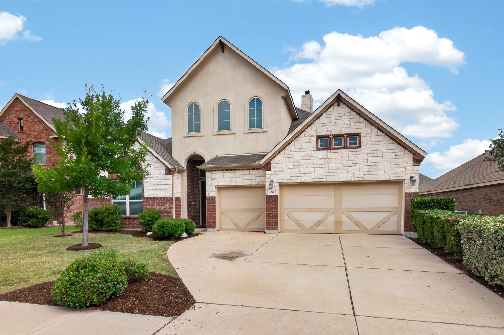 1017 Tabernash Leander, TX 78641 - Photo 2 of 38 Stucco and stone exterior featuring a two-car garage with decorative wood-finish doors, brick accents, and arched window details