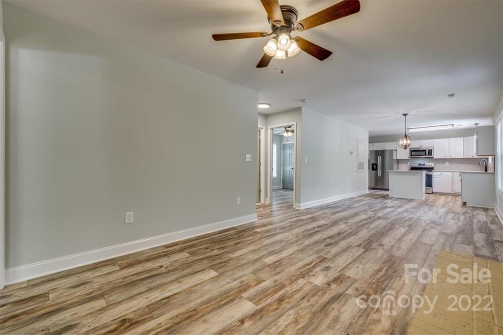 6973 Narrow Lane Road Hickory Grove, SC 29717 - Photo 9 of 35 an empty room with wooden floor a ceiling fan and kitchen view