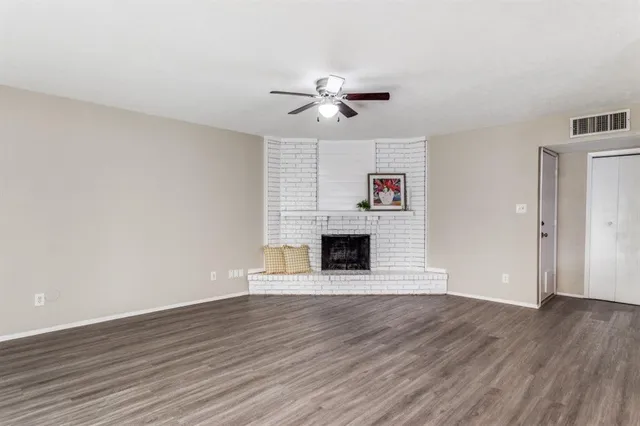 a view of an empty room with wooden floor fireplace and a window