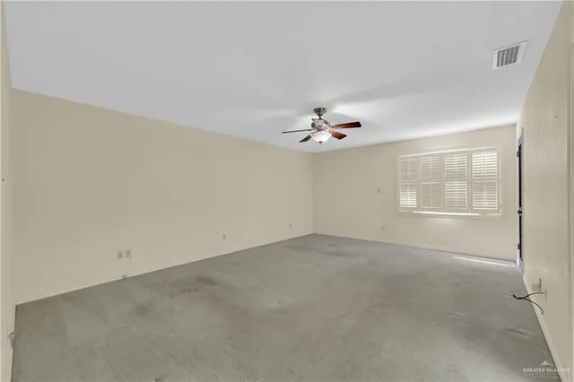 an empty room with a chandelier fan and windows