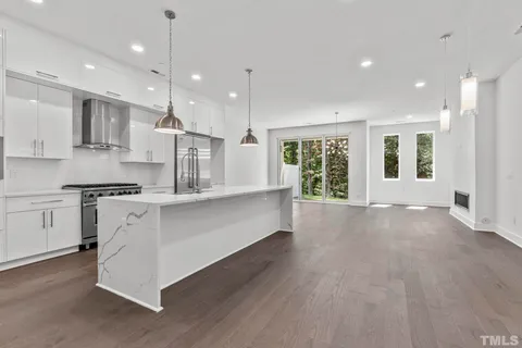 a large kitchen with stainless steel appliances granite countertop a stove a sink a refrigerator and white cabinets with wooden floor