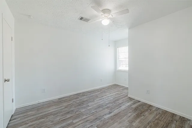 an empty room with wooden floor and fan