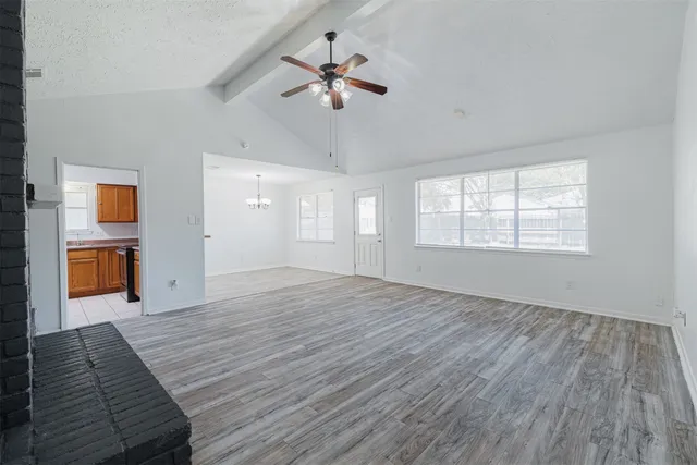 an empty room with wooden floor chandelier fan and windows