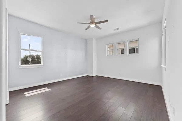 a view of an empty room with wooden floor and a ceiling fan
