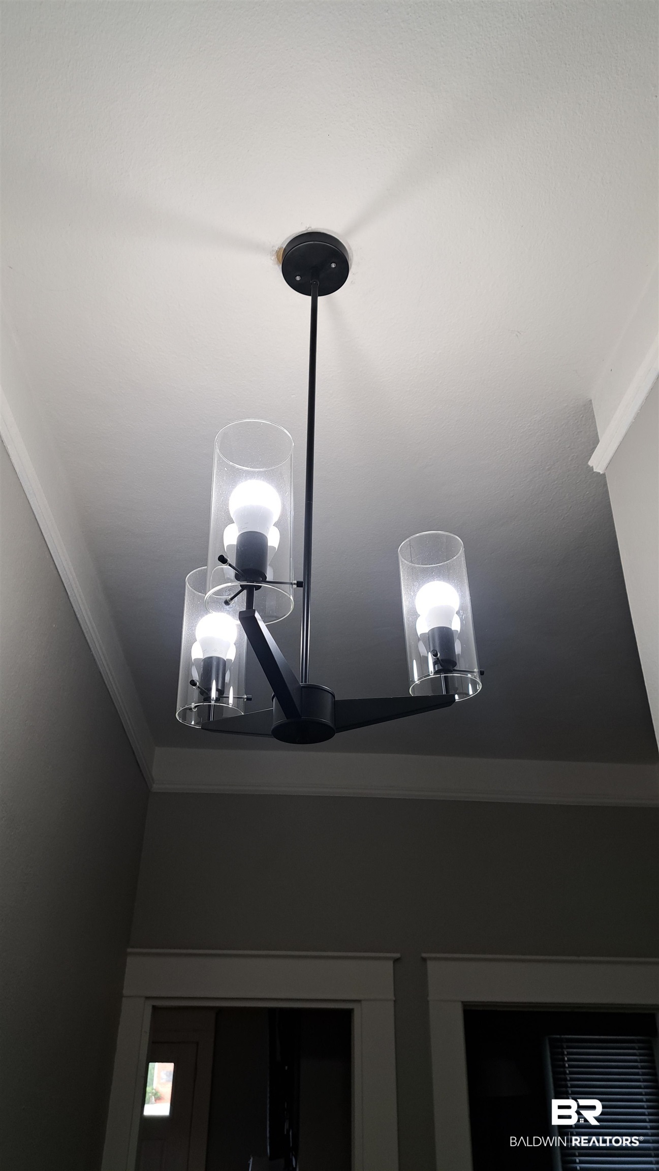 110 South Main Street Evergreen, AL 36401 - Photo 13 of 27 Modern chandelier with a matte black finish and three clear cylindrical glass shades, illuminating a neutral-toned interior with crown molding and white trim