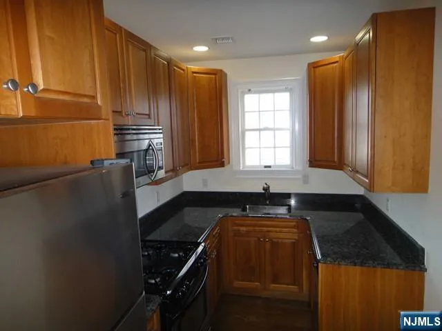 a kitchen with granite countertop a refrigerator a sink and wooden cabinets