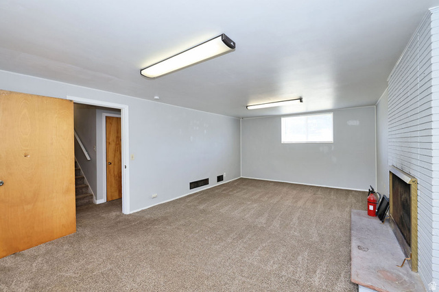 1272 Cook Street Ogden, UT 84404 - Photo 18 of 46 Spacious carpeted room featuring a white brick fireplace with a stone hearth, a high window, and overhead strip lighting