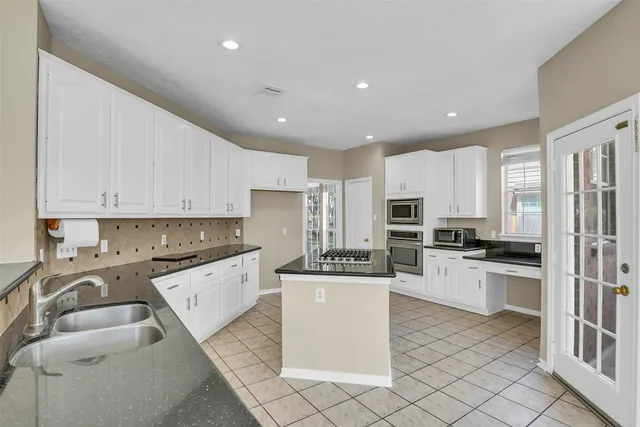 a kitchen with stainless steel appliances granite countertop a stove top oven a sink a refrigerator and white cabinets