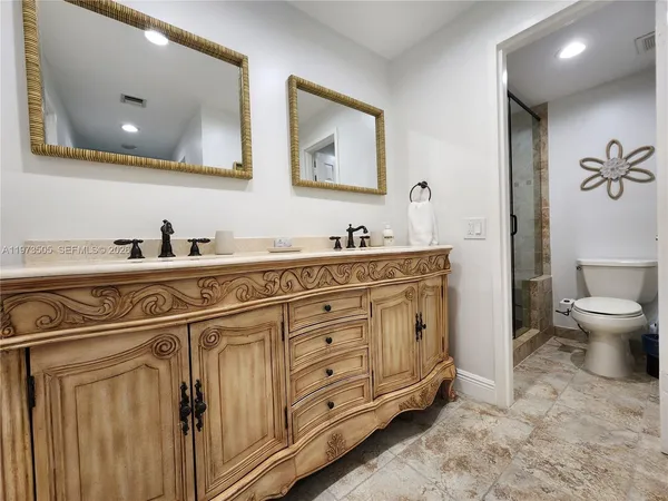 a spacious bathroom with double sink a toilet a mirror and shower
