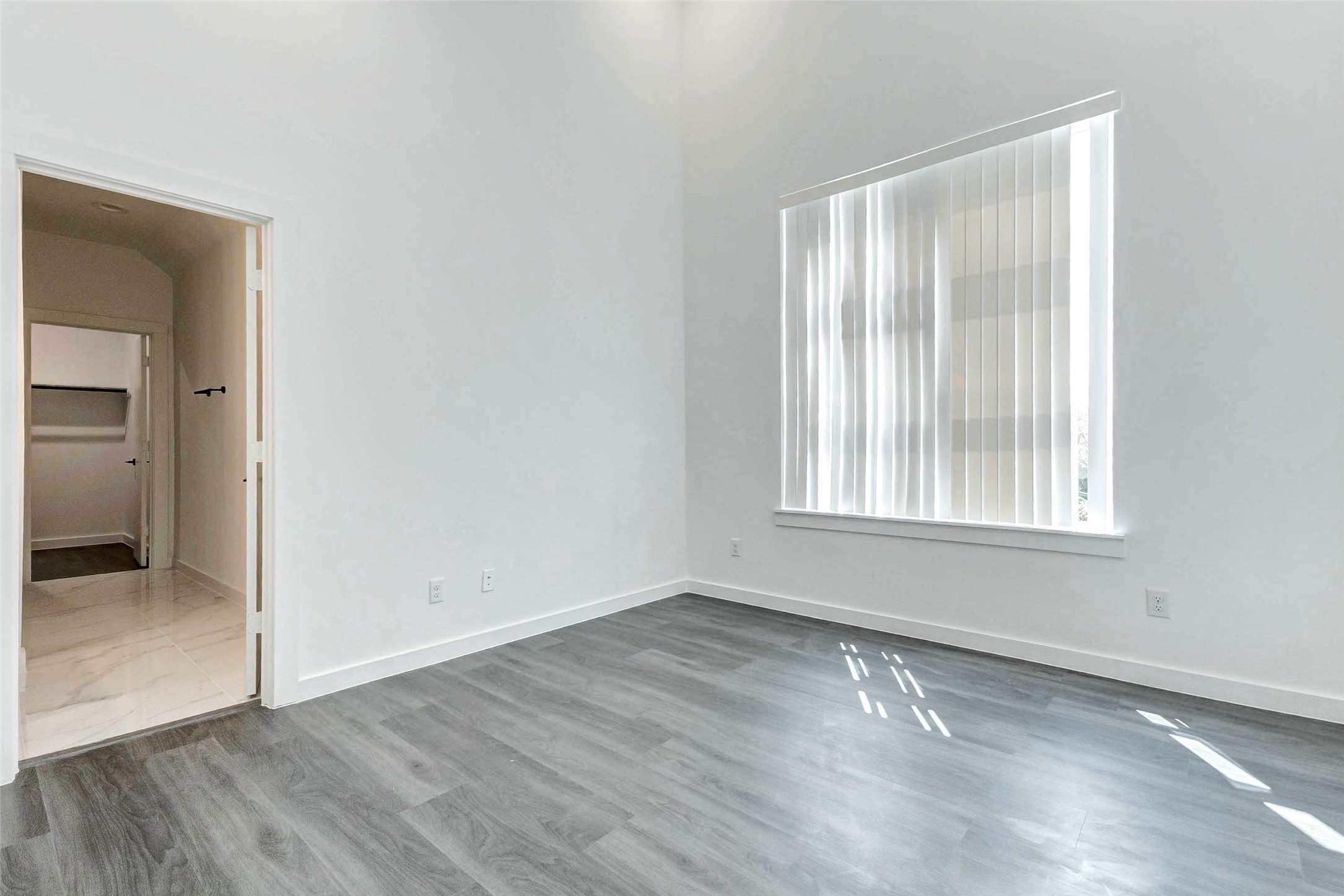 6017 Beall Street Houston, TX 77091 - Photo 24 of 33 oaring ceilings, wide-plank flooring, and generous natural light define this serene primary suite. A large window with vertical blinds adds privacy, while the ensuite bath and walk-in closet are just steps away.
