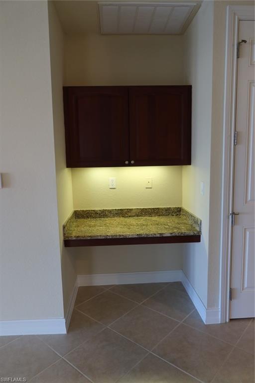 7168 Lemuria Circle, Unit 1701 Naples, FL 34109 - Photo 16 of 39 Built-in desk area featuring a stone-finish countertop, under-cabinet lighting, upper cabinetry, and tile flooring