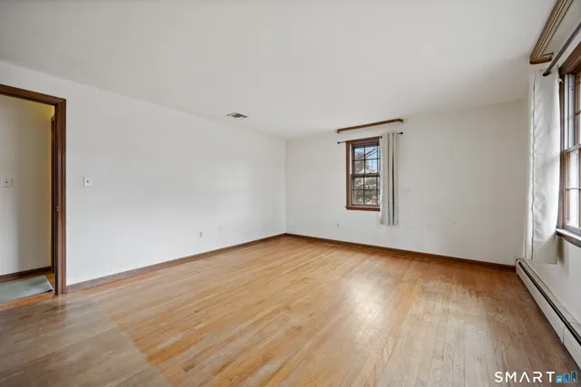 a view of an empty room with wooden floor and a window