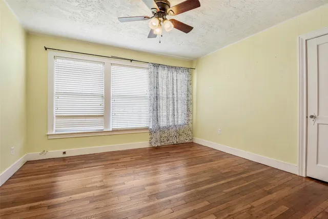 an empty room with wooden floor fan and windows