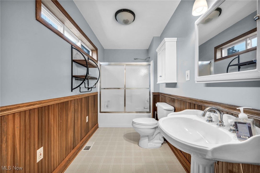 4743 Broadale Road Cleveland, OH 44109 - Photo 22 of 32 Full bath featuring a wainscoted wall, wood walls, bath / shower combo with glass door, and light flooring
