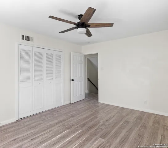 a view of an empty room with wooden floor and a ceiling fan