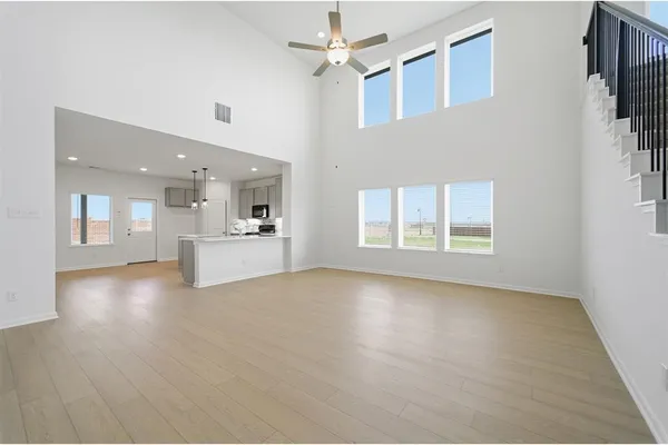 a view of an empty room with a kitchen and chandelier fan