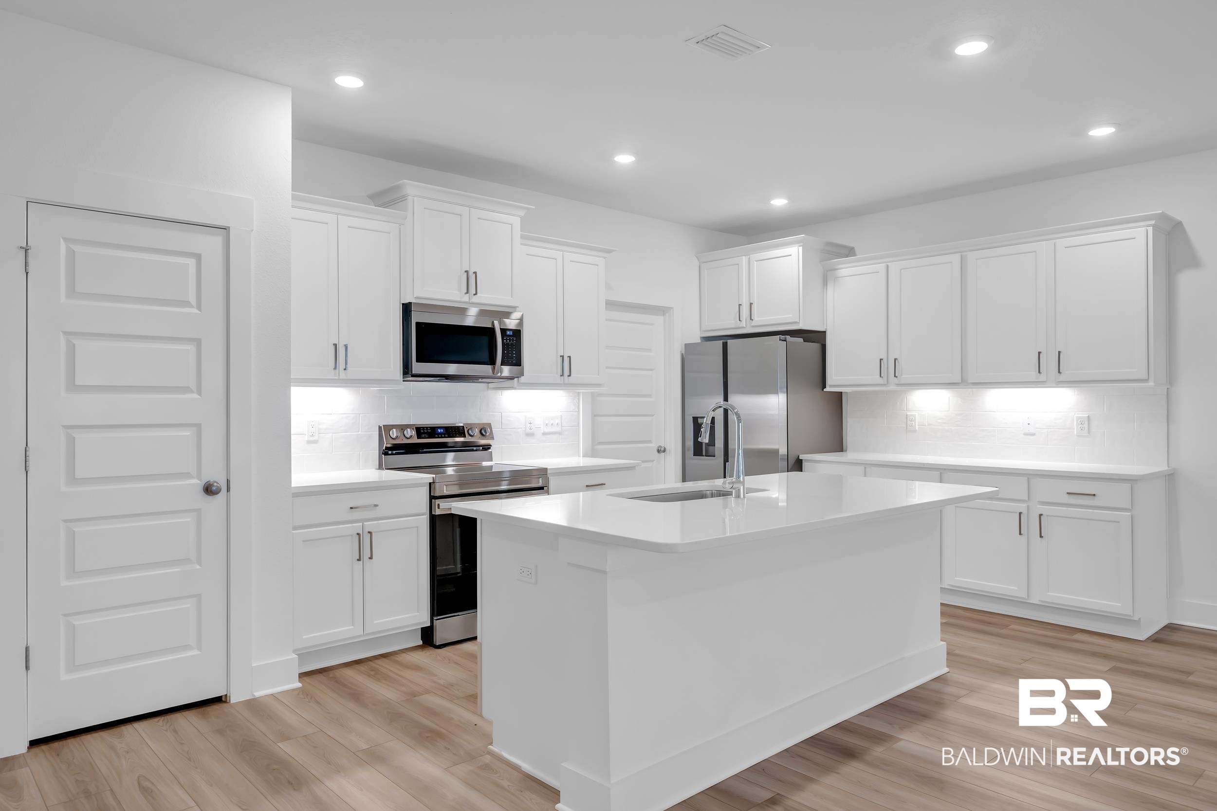 9933 Weller Cove Foley, AL 36535 - Photo 8 of 36 Modern kitchen featuring an expansive center island, white shaker cabinetry, stainless steel appliances, and wood-finish flooring