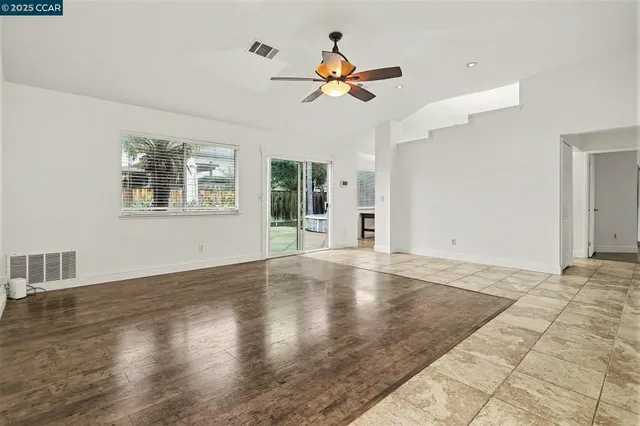 a view of an empty room with wooden floor and a ceiling fan