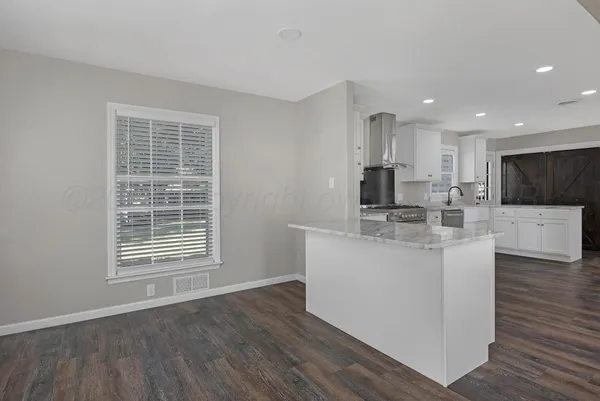 a kitchen with stainless steel appliances granite countertop a sink a microwave a refrigerator a stove and white cabinets with wooden floor