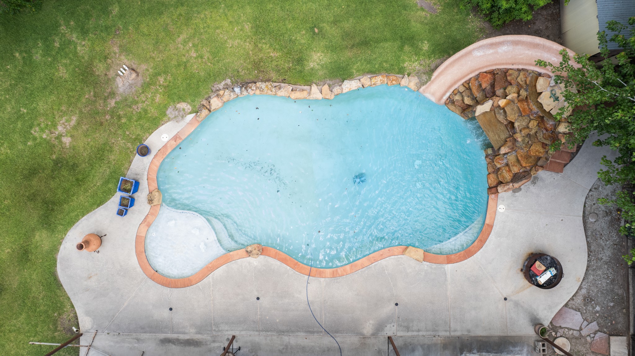 15602 Fir Road Santa Fe, TX 77517 - Photo 31 of 42 Stunning aerial view of the resort-style pool showcasing the custom rock waterfall slide, expansive concrete decking, and generous outdoor entertaining space. The freeform design and surrounding green space create a true backyard oasis.