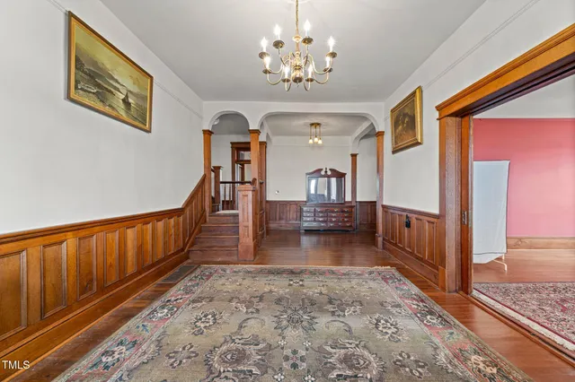 a view of a hallway with wooden floor staircase and a kitchen space with a chandelier