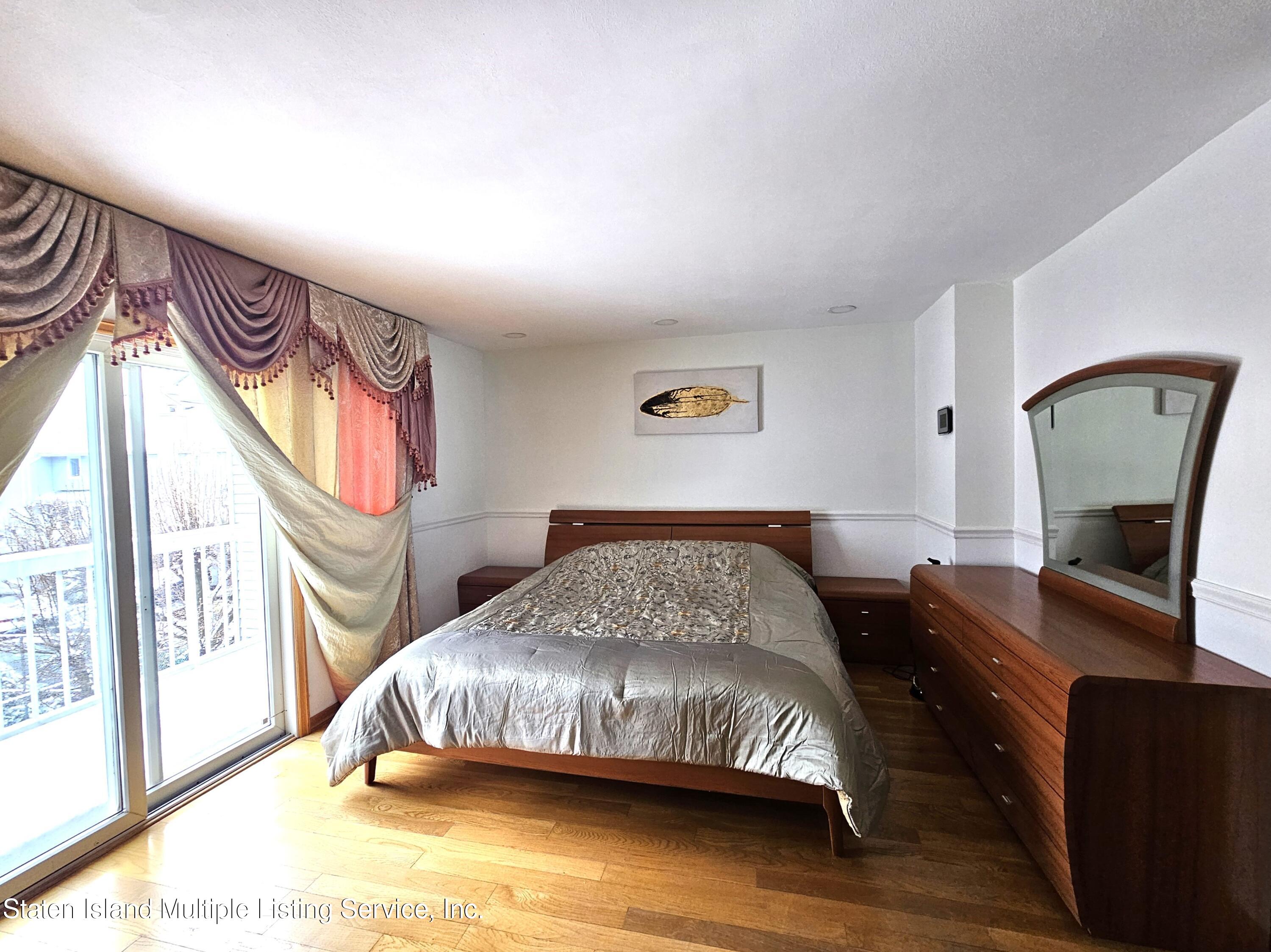 142 Commodore Drive Staten Island, NY 10309 - Photo 18 of 26 a bedroom with a bed a mirror on the dresser and a large window