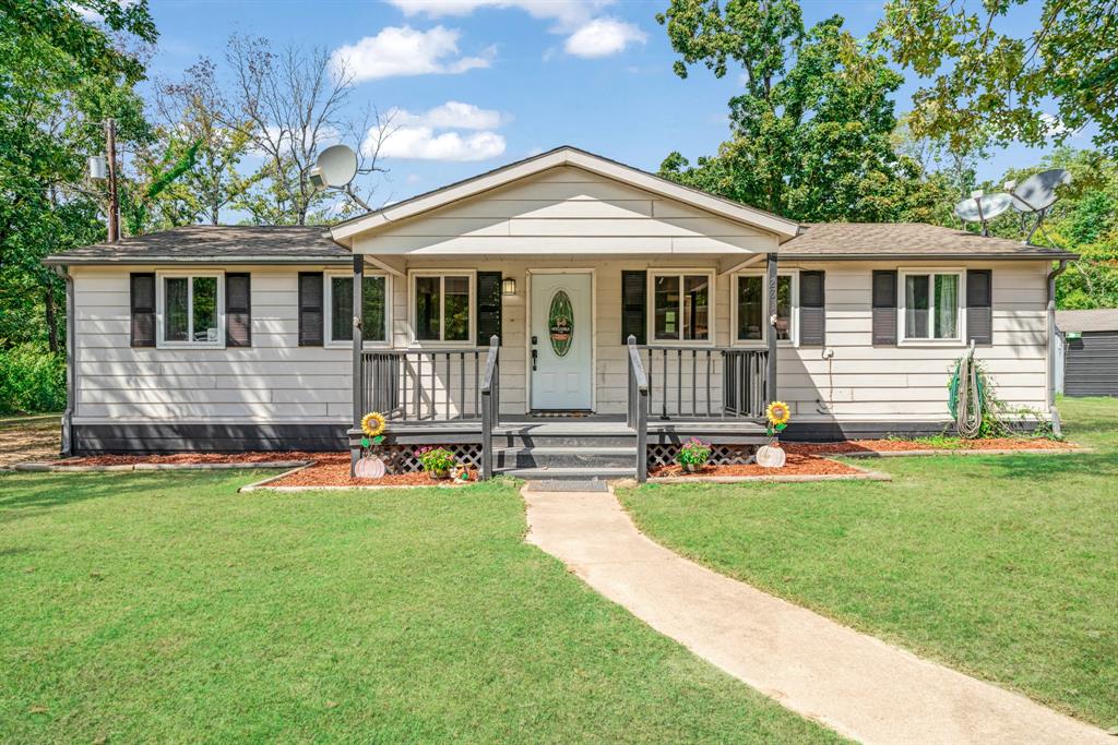 Ranch-style house featuring covered porch, a front lawn, and a shingled roof