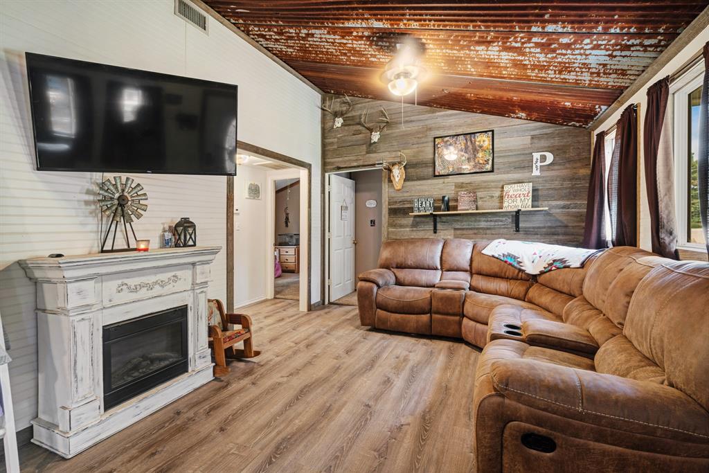 28 Private Road Sumner, TX 75486 - Photo 3 of 17 Living area featuring vaulted ceiling, wood walls, wood finished floors, a glass covered fireplace, and a ceiling fan