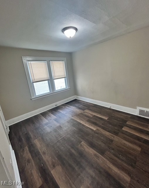 Empty room with a textured ceiling and dark wood-type flooring