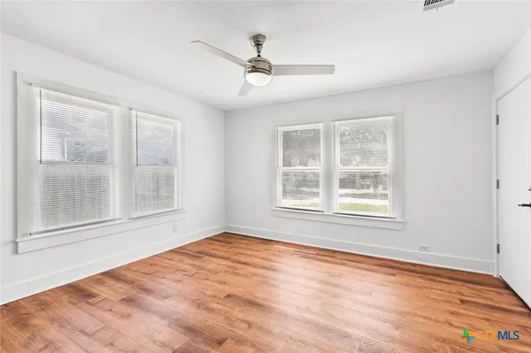 an empty room with wooden floor ceiling fan and windows