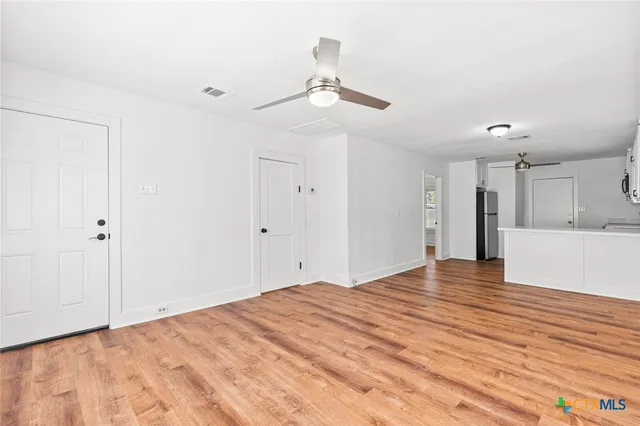 a view of an empty room with wooden floor and a ceiling fan