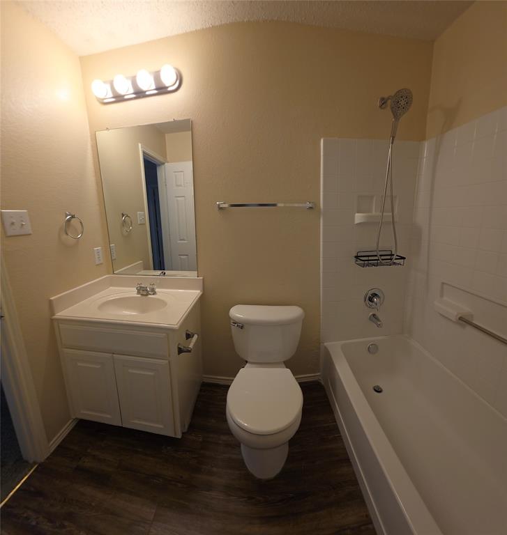 2820 Deer Ridge Drive Rockwall, TX 75032 - Photo 21 of 36 Full bathroom featuring a white vanity with integrated sink, wood-finish flooring, a toilet, and a bathtub with a tiled surround