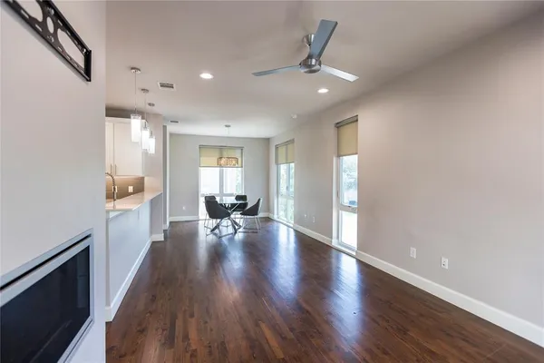 a view of an empty room and kitchen with wooden floor